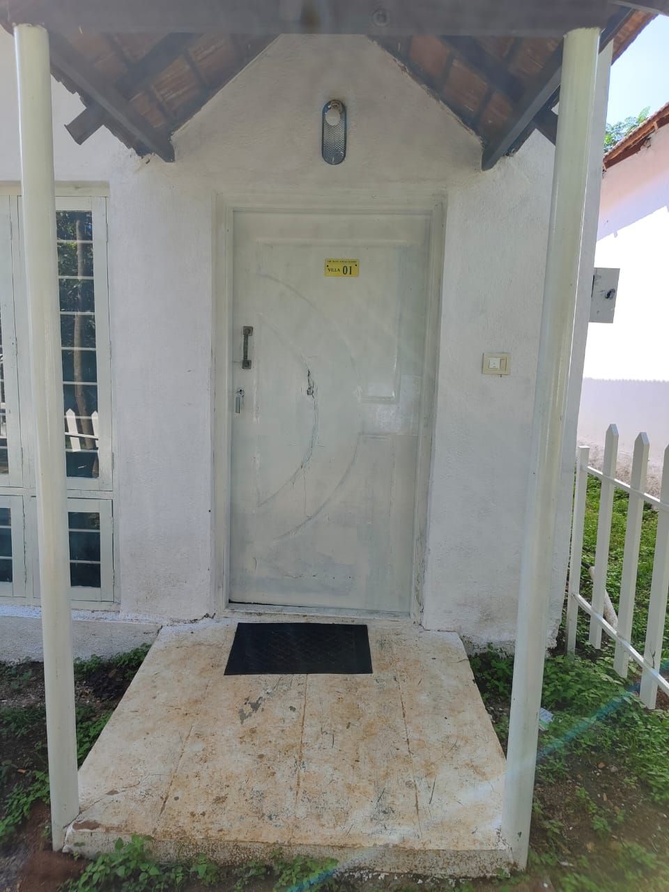 A white door with a yellow sign, a small porch with a black mat, and a white fence.