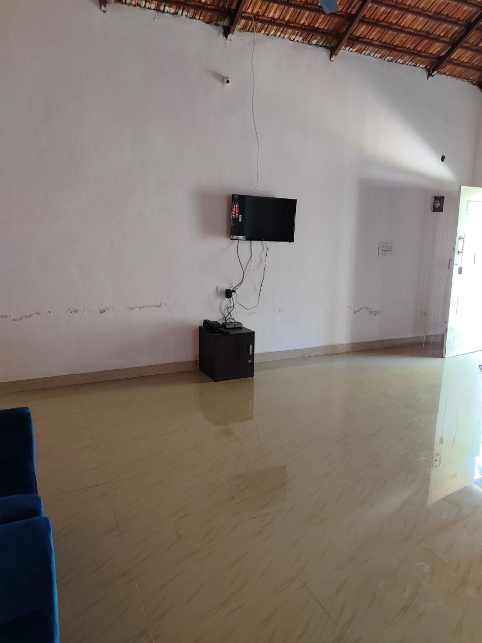 A spacious room with a tiled floor, a mounted television, and a power strip on the wall.