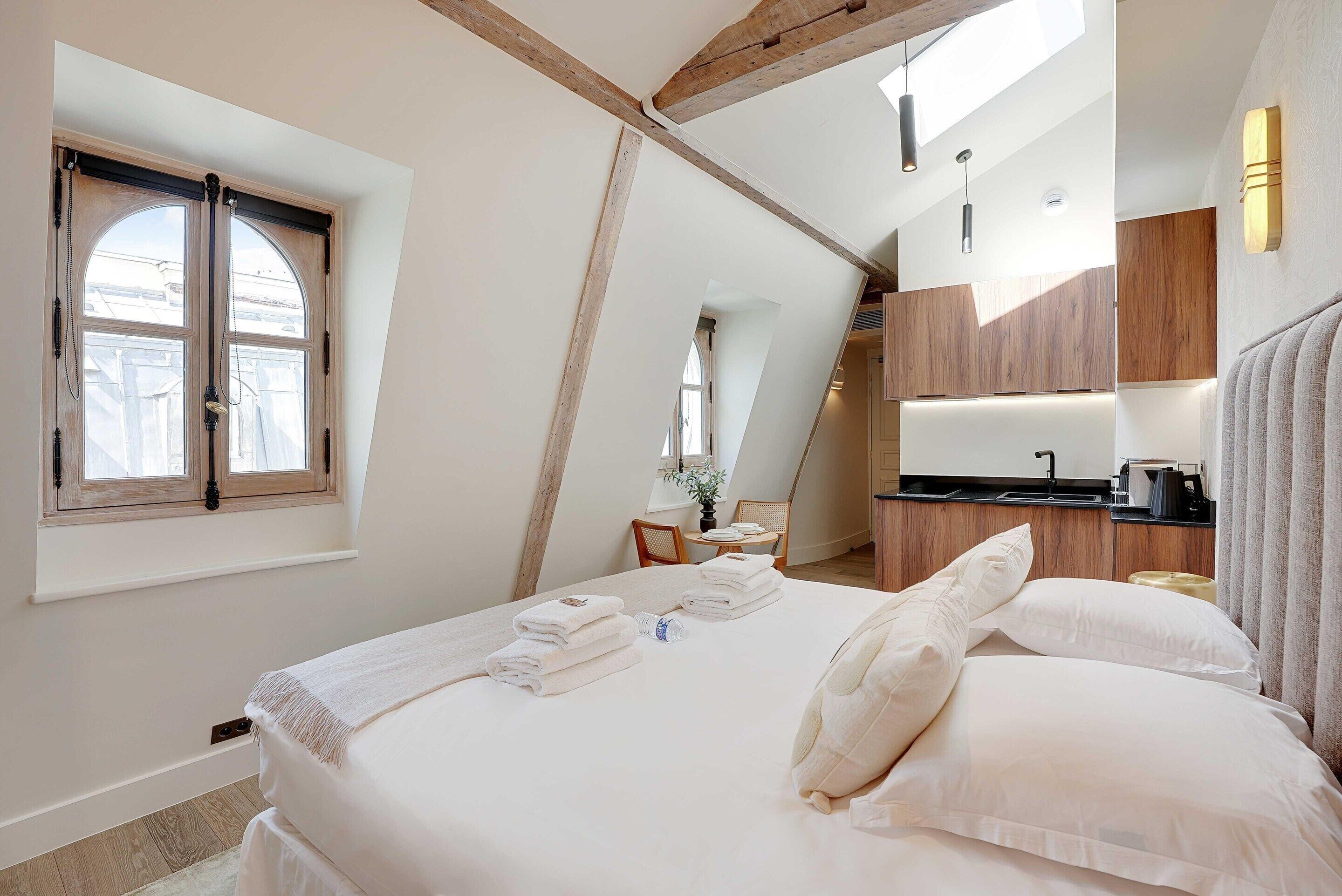 Un dormitorio con una cama grande, un tragaluz, techo de madera y una pequeña kitchenette.