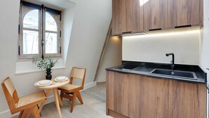 Une cuisine de taille réduite, dotée de meubles en bois, d’un plan de travail noir et d’une fenêtre donnant sur des immeubles.