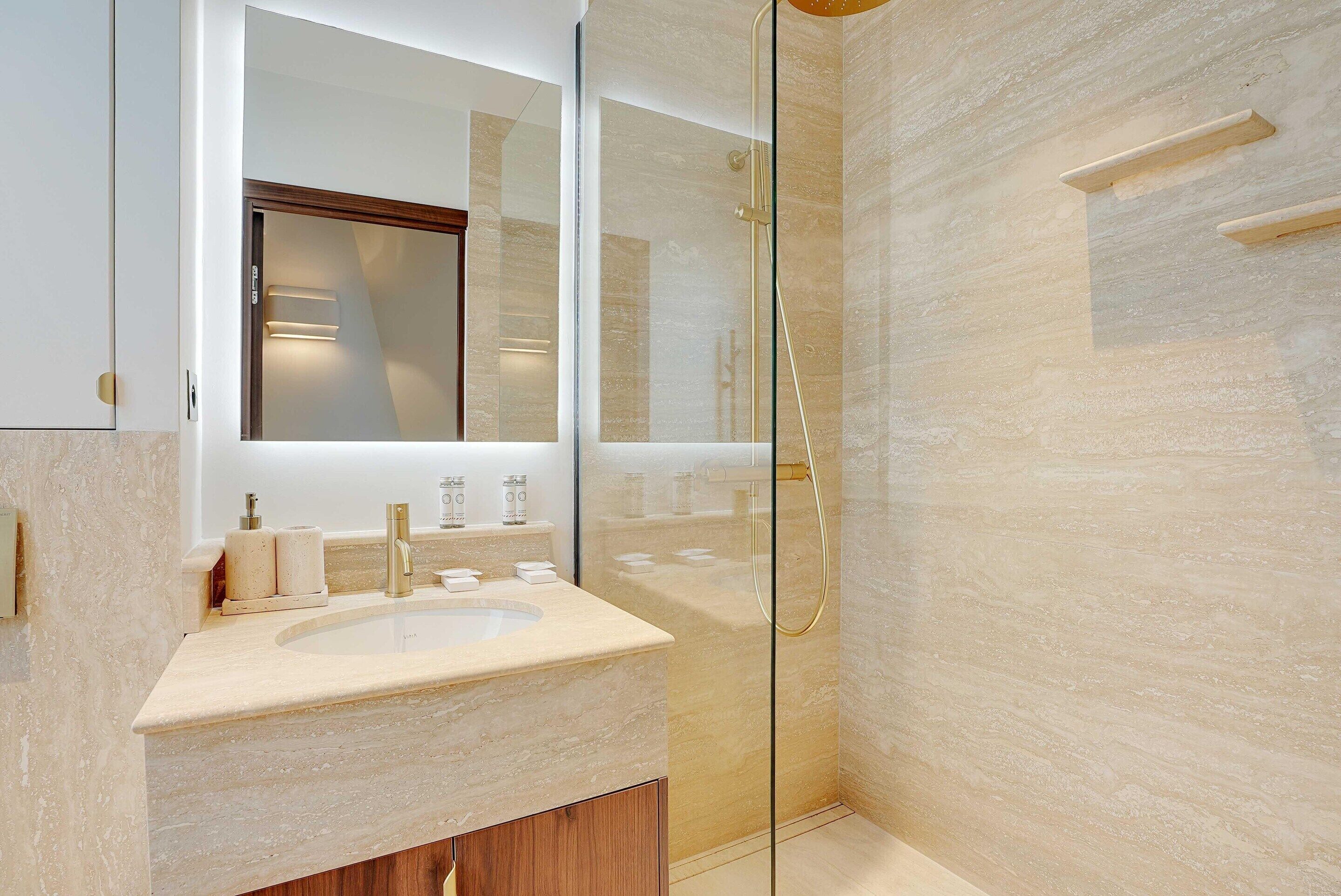 Un baño moderno con ducha acristalada, un espejo grande y encimera de mármol.
