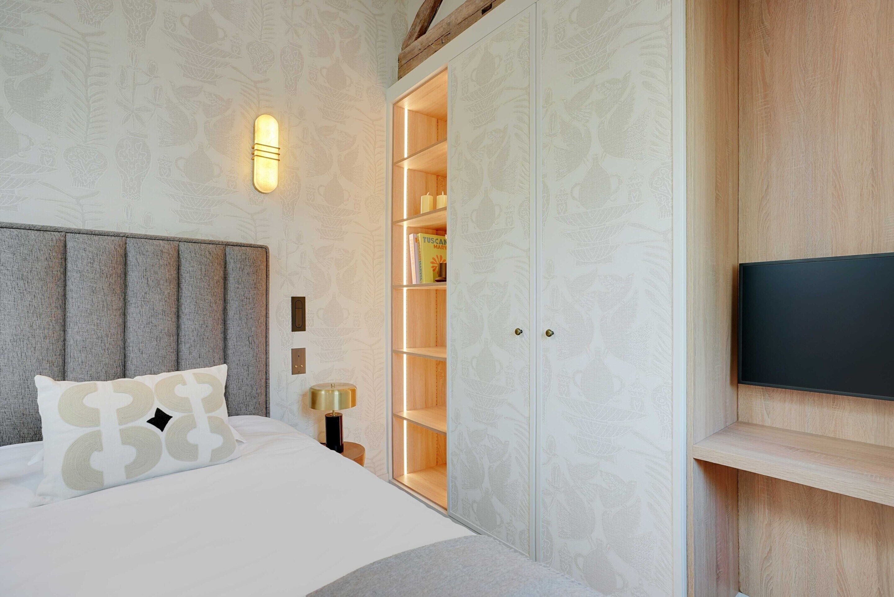 Un dormitorio con cama, mesita de noche, televisor de pared y armario empotrado con estantes.