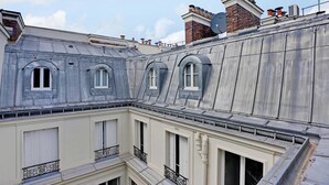 Un immeuble à plusieurs étages, doté d’un toit gris, de nombreuses cheminées et d’un balcon orné de balustrades décoratives.