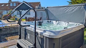 A hot tub with a metal ladder, a wooden deck, and a view of a house and garden.