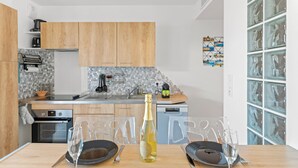 A modern kitchen with wooden cabinets, a built-in oven, and a dining area with a table set for two. - Le Nid Bleu - Entre Mer et Montagne (Grosseto-Prugna)