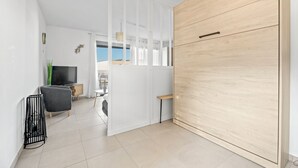 A modern living room with a TV, a grey sofa, a wooden cabinet, and a white partition. - Le Nid Bleu - Entre Mer et Montagne (Grosseto-Prugna)