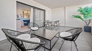 A modern outdoor dining area with a table and chairs, a sliding glass door leading to a kitchen, and a potted tree. - Le Nid Bleu - Entre Mer et Montagne (Grosseto-Prugna)