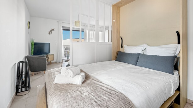 A modern hotel room with a large bed, a TV, a desk, and a view of the sky. - Le Nid Bleu - Entre Mer et Montagne (Grosseto-Prugna)