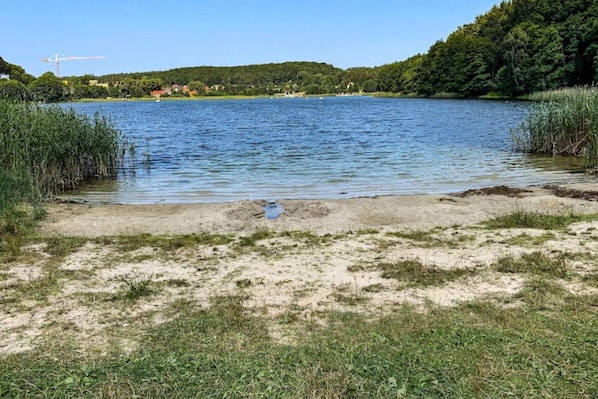 Un lago con orilla arenosa, rodeado de vegetación y una grúa de construcción a lo lejos.