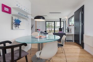 Zona pranzo moderna con tavolo in vetro, sedie bianche e lampadario nero.