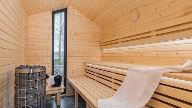 Una sauna con bancos de madera, pared de piedra y ventana.