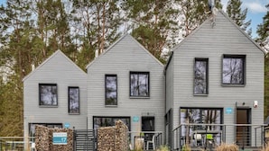 A modern two-story building with a stone wall entrance and a metal gate. - Holiday Home by Lake Wisełka with Sauna (Wiselka)