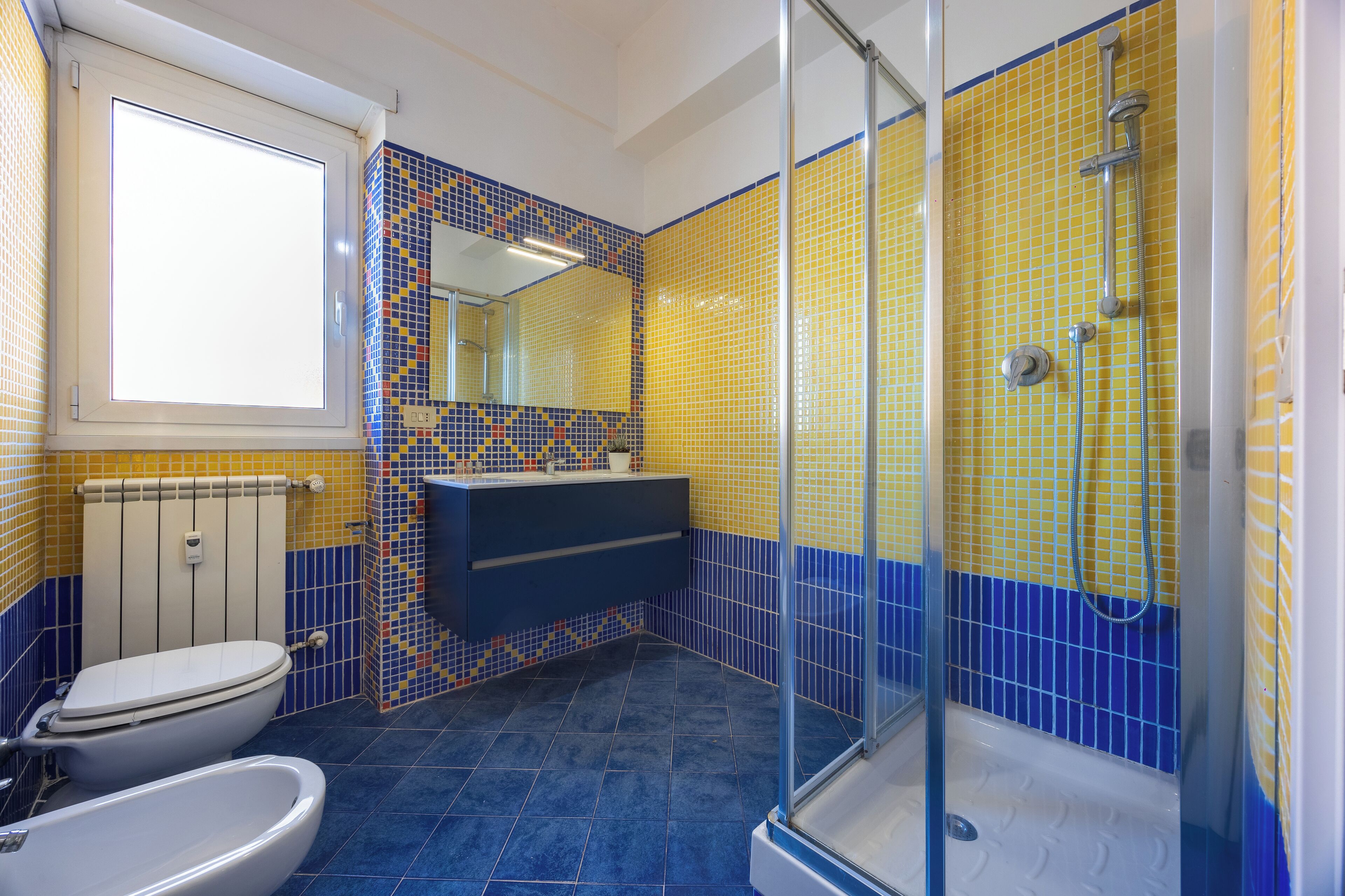 Une salle de bain équipée de toilettes, d’un bidet et d’une douche avec une porte en verre.