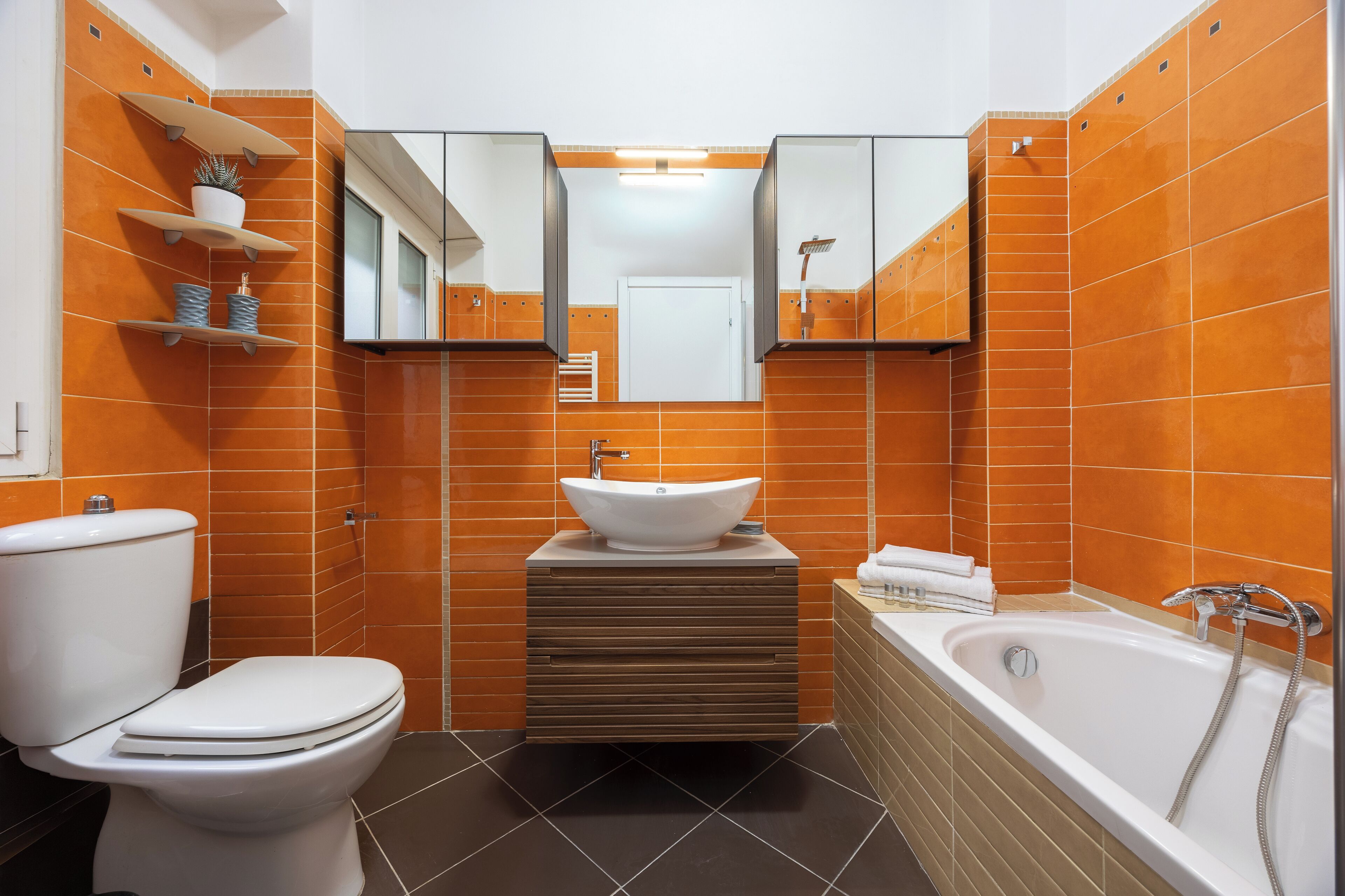 A modern bathroom with a white toilet, a sink with a mirror above, and a bathtub.
