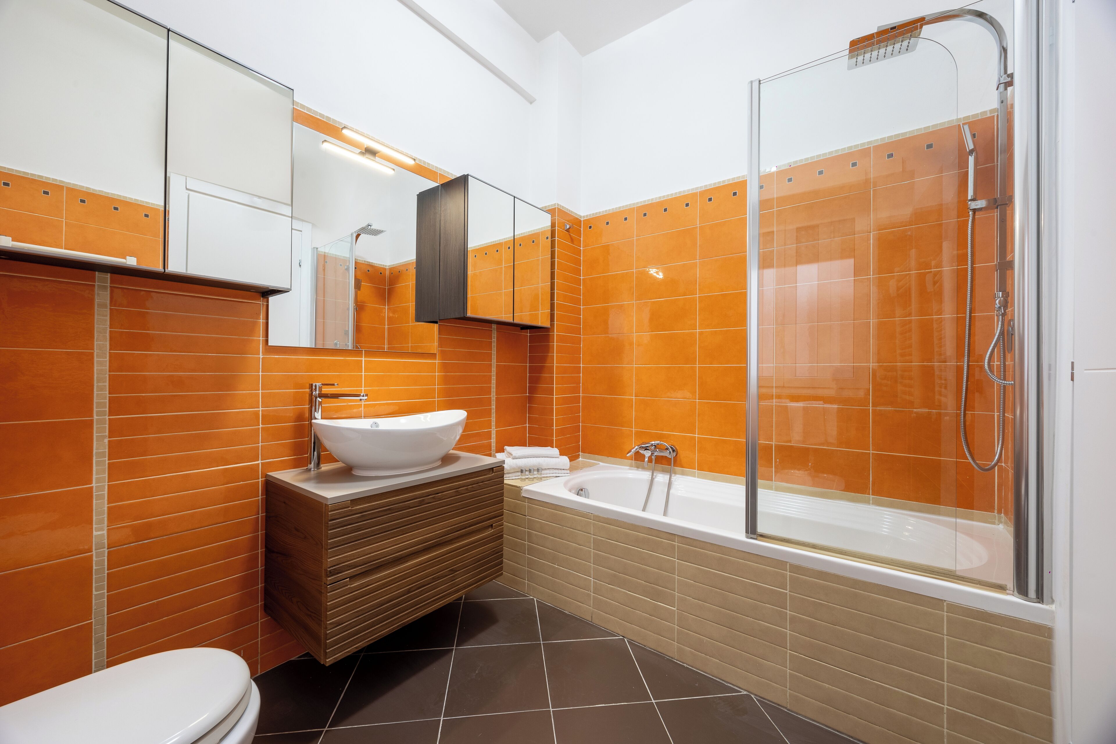 A modern bathroom with a white toilet, a wooden vanity with a white sink, and a glass-enclosed shower area.