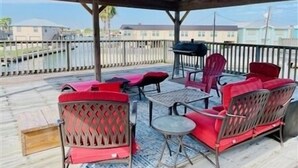 A covered outdoor seating area with red chairs and a table, overlooking a body of water.
