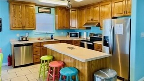 A kitchen with wooden cabinets, stainless steel appliances, a central island with stools, and a trash can.