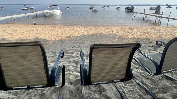 Une plage avec deux rangées de chaises longues orientées vers la mer, une jetée en bois et plusieurs bateaux sur l’eau.