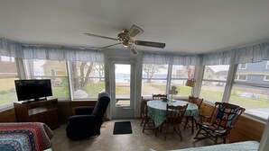 Une véranda avec un ventilateur de plafond, un téléviseur, une table à manger avec des chaises et deux canapés.