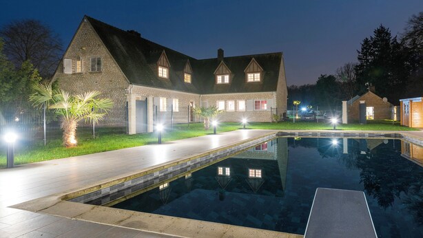 Un edificio in pietra con piscina, un vialetto lastricato e un'illuminazione esterna notturna.