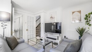 Un soggiorno moderno con televisore a schermo piatto, divani grigi, un tavolino da caffè in vetro e una scala che conduce al bagno.
