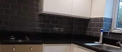 Une cuisine moderne avec des armoires blanches, un dosseret de carrelage noir, une hotte de cuisinière en acier inoxydable, un four encastré, un évier et un lave-linge.