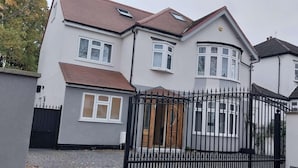 Une maison à deux étages, avec une façade grise, un portail en métal noir et un toit recouvert de tuiles rouges.