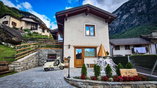 A two-story house with a stone staircase, a scooter parked in front, and a sign indicating a vacation rental. - Cozy vacation home surrounded by nature, pets allowed. (San Giacomo Filippo)