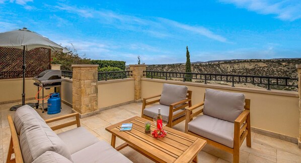 A rooftop terrace with a grill, seating, and a view of the landscape.