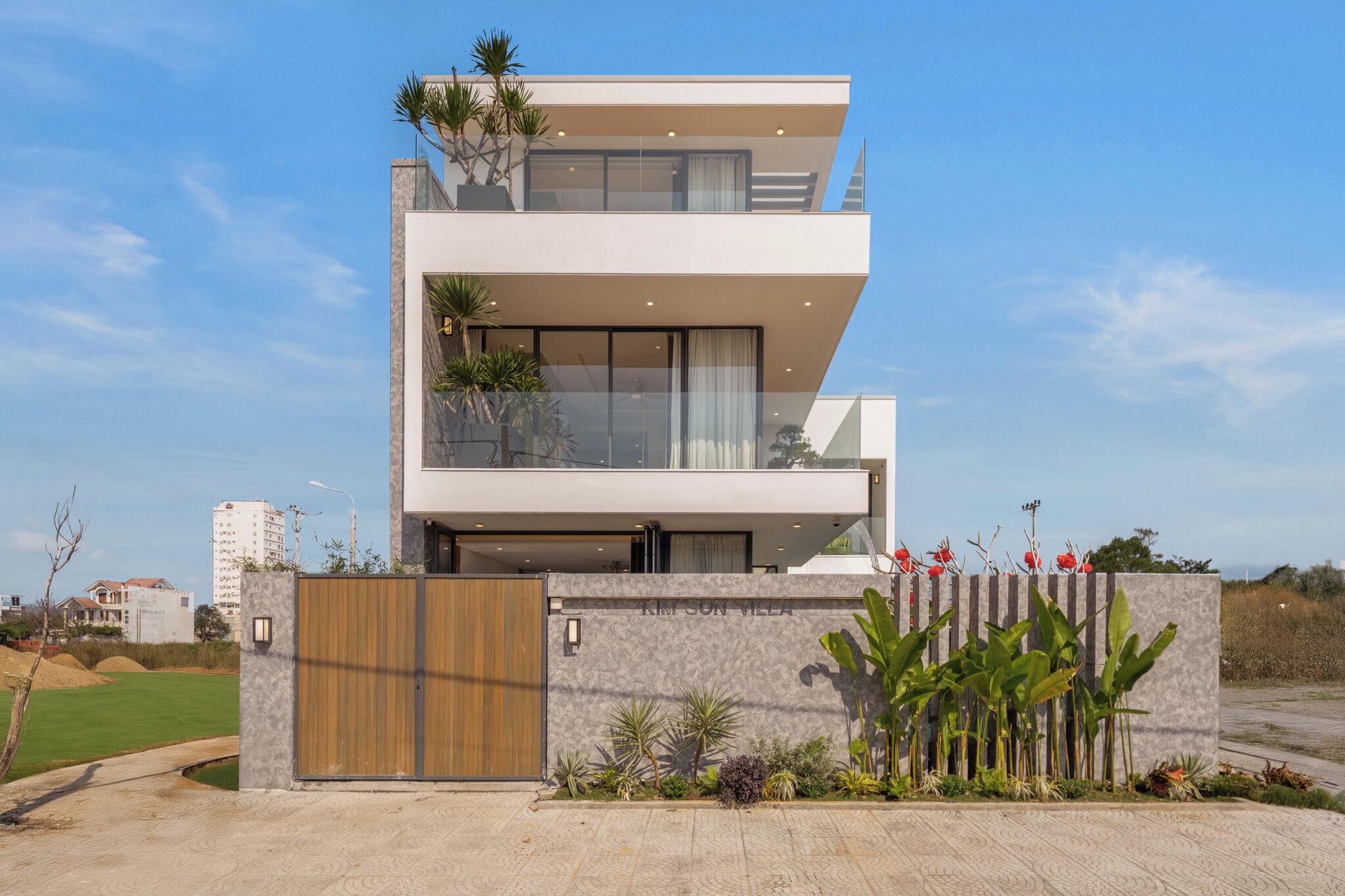 A modern two-story house with a balcony, a gated entrance, and a well-maintained garden.
