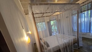 Une pièce avec un lit recouvert d’un dais léger et transparent, un banc en bois et une vue sur la verdure à l’extérieur.