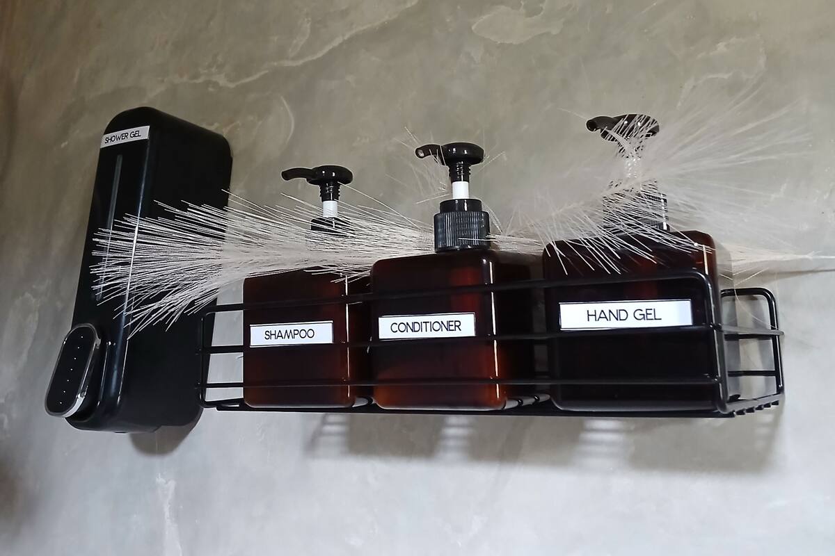 Dispensador montado en la pared con botellas etiquetadas de gel de ducha, gel hidroalcohólico, champú y acondicionador.