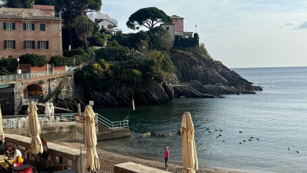 A coastal scene with a rocky cliff, a beach, and a café area with outdoor seating.