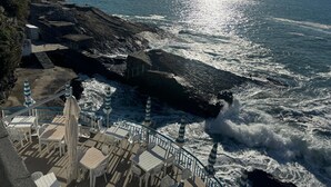 A coastal deck with outdoor seating and a rocky shoreline.