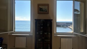 A room with large bay windows overlooking the sea, a radiator, and a cabinet with dishes.