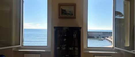 Una habitación con amplios ventanales que dan al mar, un radiador y un mueble con vajilla.