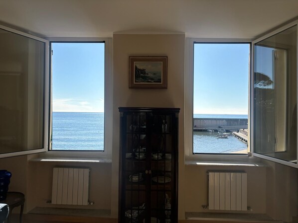 A room with large bay windows overlooking the sea, a radiator, and a cabinet with dishes.
