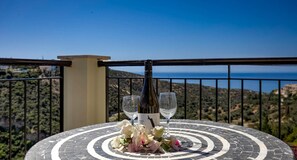 A table with a bottle and two glasses, set on a balcony with a scenic view.