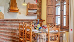 Un coin repas avec un mur en briques, des chaises en bois, une table dressée avec des assiettes, des verres et un panier de fruits.