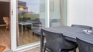 Ein modernes Wohnzimmer mit einer Glastür, die zu einem Außenbereich führt. Innen befinden sich ein Esstisch mit Stühlen, eine Couch und ein kleiner Couchtisch.