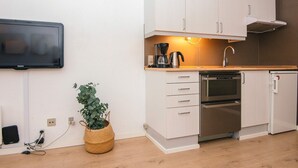Eine kompakte Küchenzeile mit weißen Schränken, einem eingebauten Backofen, einer Kaffeemaschine und einem an der Wand befestigten Flachbildfernseher.