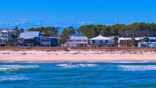 A beachfront property with multiple buildings, a sandy beach, and a clear blue sky. - Life's A Beach - Pet Friendly, Private Pool, Beach Views, Across from Beach! (St George Island)