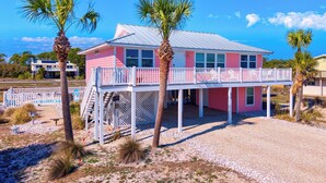 A pink beach house with a balcony, palm trees, and a clear blue sky. - Life's A Beach - Pet Friendly, Private Pool, Beach Views, Across from Beach! (St George Island)