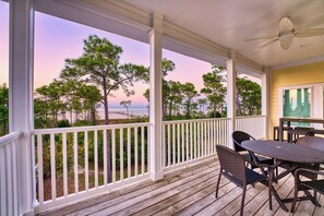 A covered outdoor area with a table and chairs, a ceiling fan, and a view of trees and a beach. - Bay Breeze - Pet Friendly, Bay View, Community Pool & Dock! (St George Island)