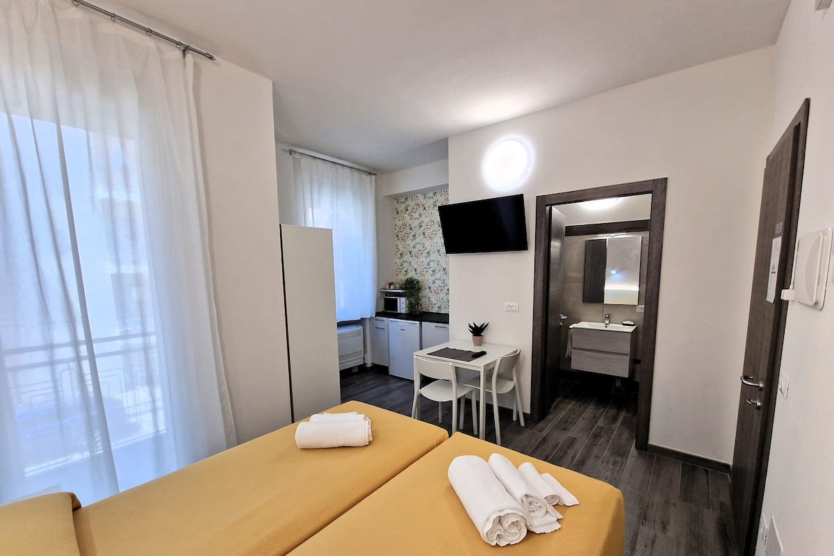 Camera d'albergo con un letto, una scrivania, una sedia, un tavolino, una TV, uno specchio e un bagno.
