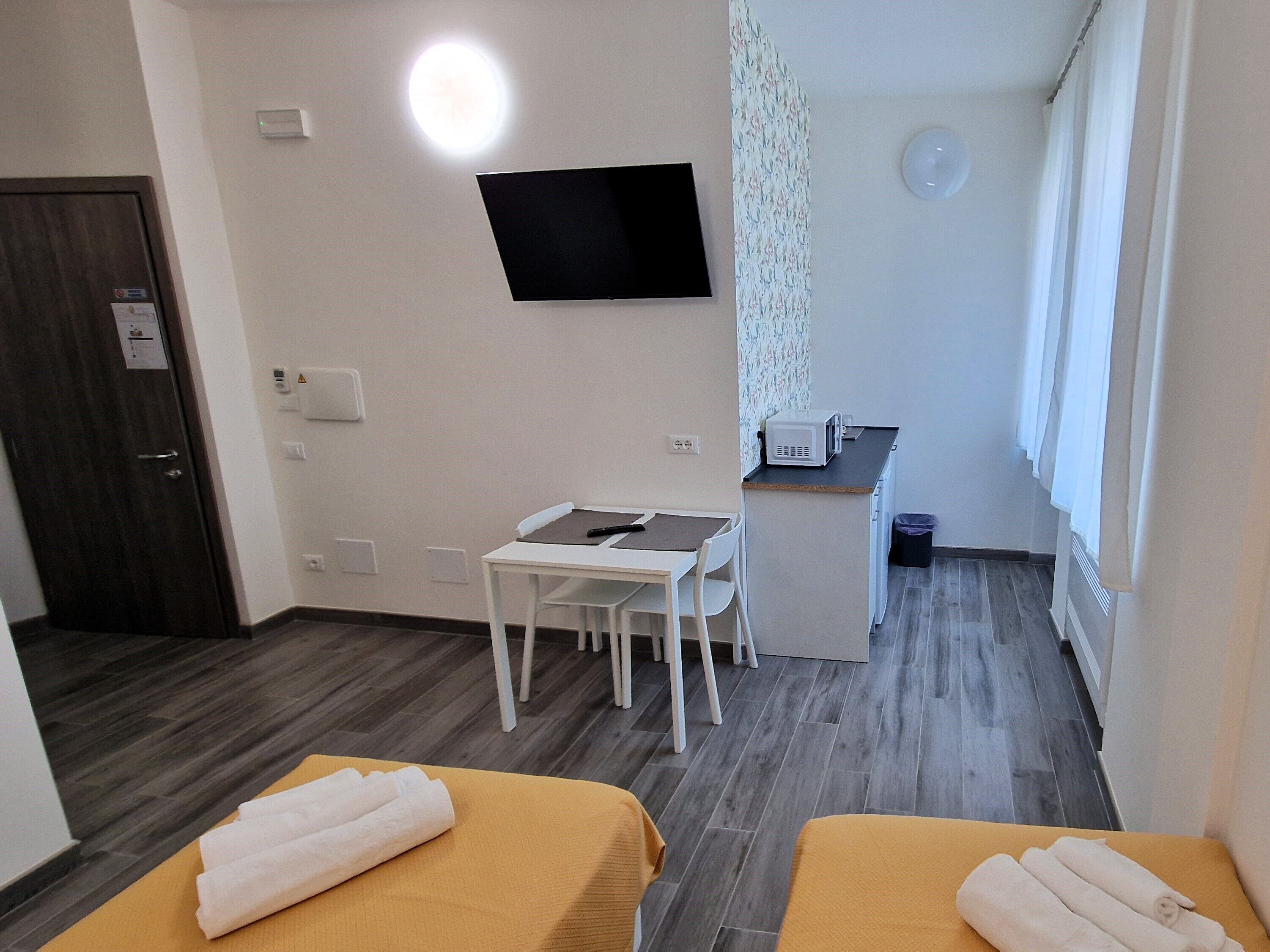 Una habitación de hotel con dos camas, un escritorio, una silla, un microondas y un televisor en la pared.