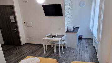 Una habitación de hotel con dos camas, un escritorio, una silla, un microondas y un televisor en la pared.