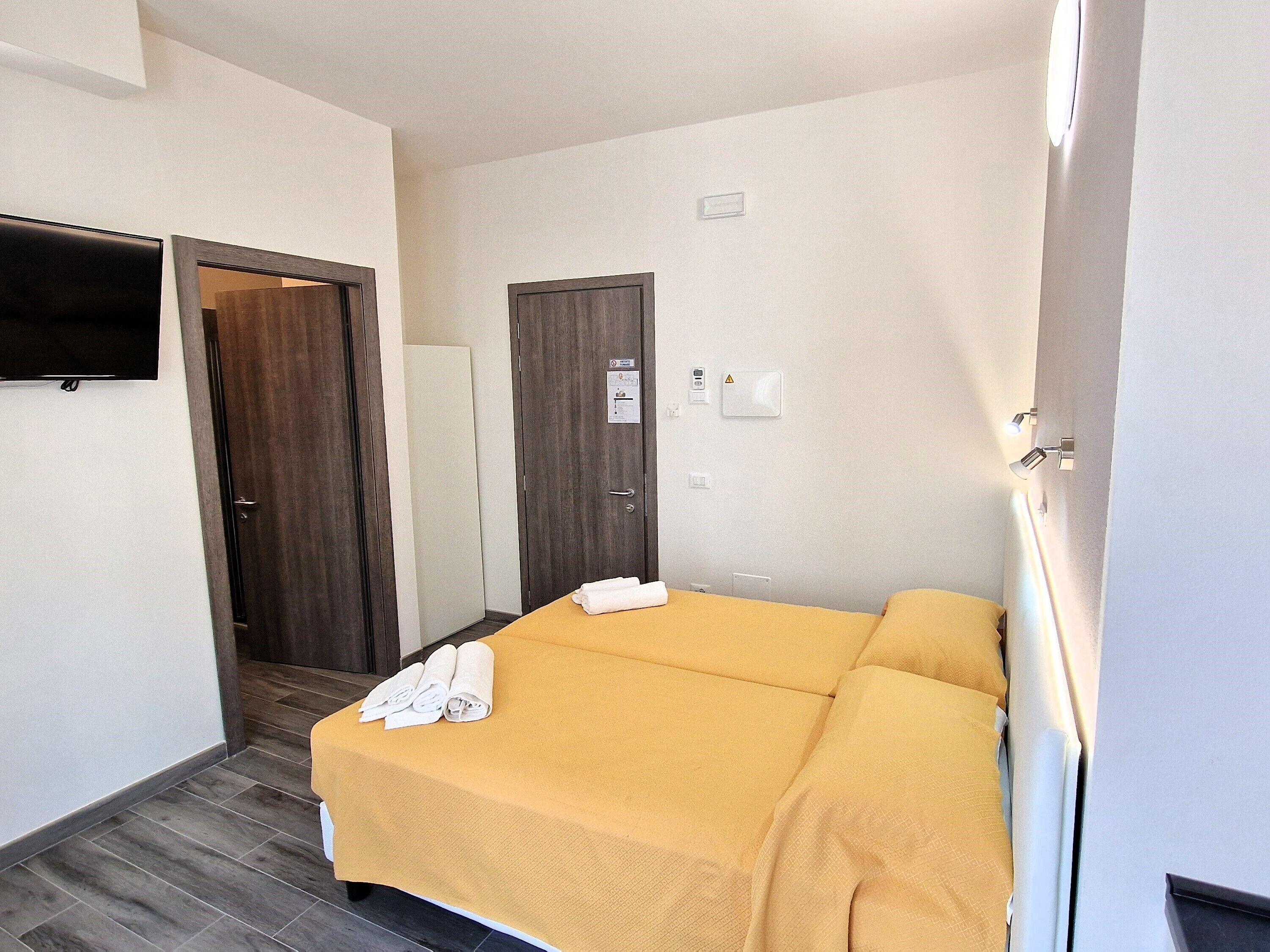 A hotel room with a bed, a TV mounted on the wall, and a door leading to another room.