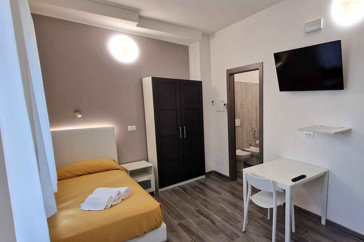 Una camera d'albergo con un letto, una scrivania, una televisione, un armadio e un bagno.