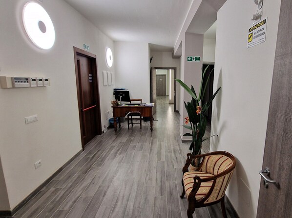 A hotel hallway with a reception desk, a chair, a potted plant, and a sign indicating an elevator. - Belfiore Alloggi Turistici (Vicenza)